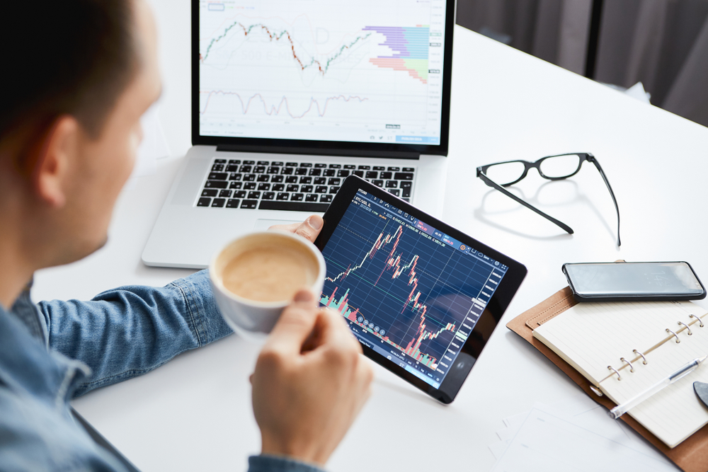 A man drinking coffee and looking at a graph on a tablet