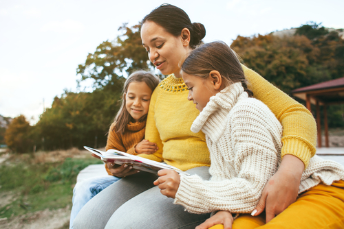 Mom reading a book to her children outdoors in autumn.