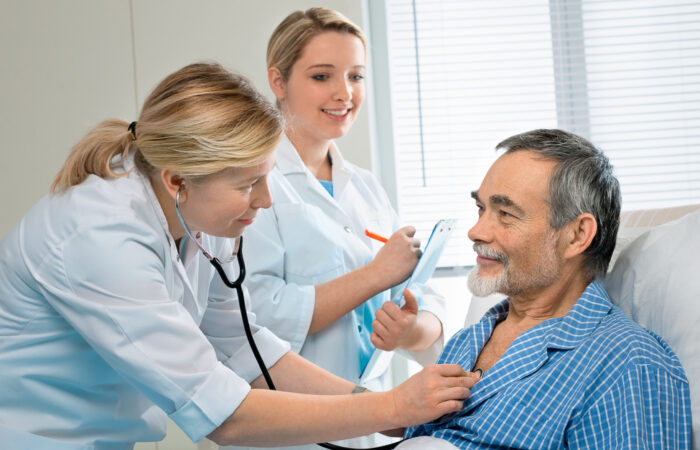 Doctor listening to patient's heartbeat while nurse takes note.